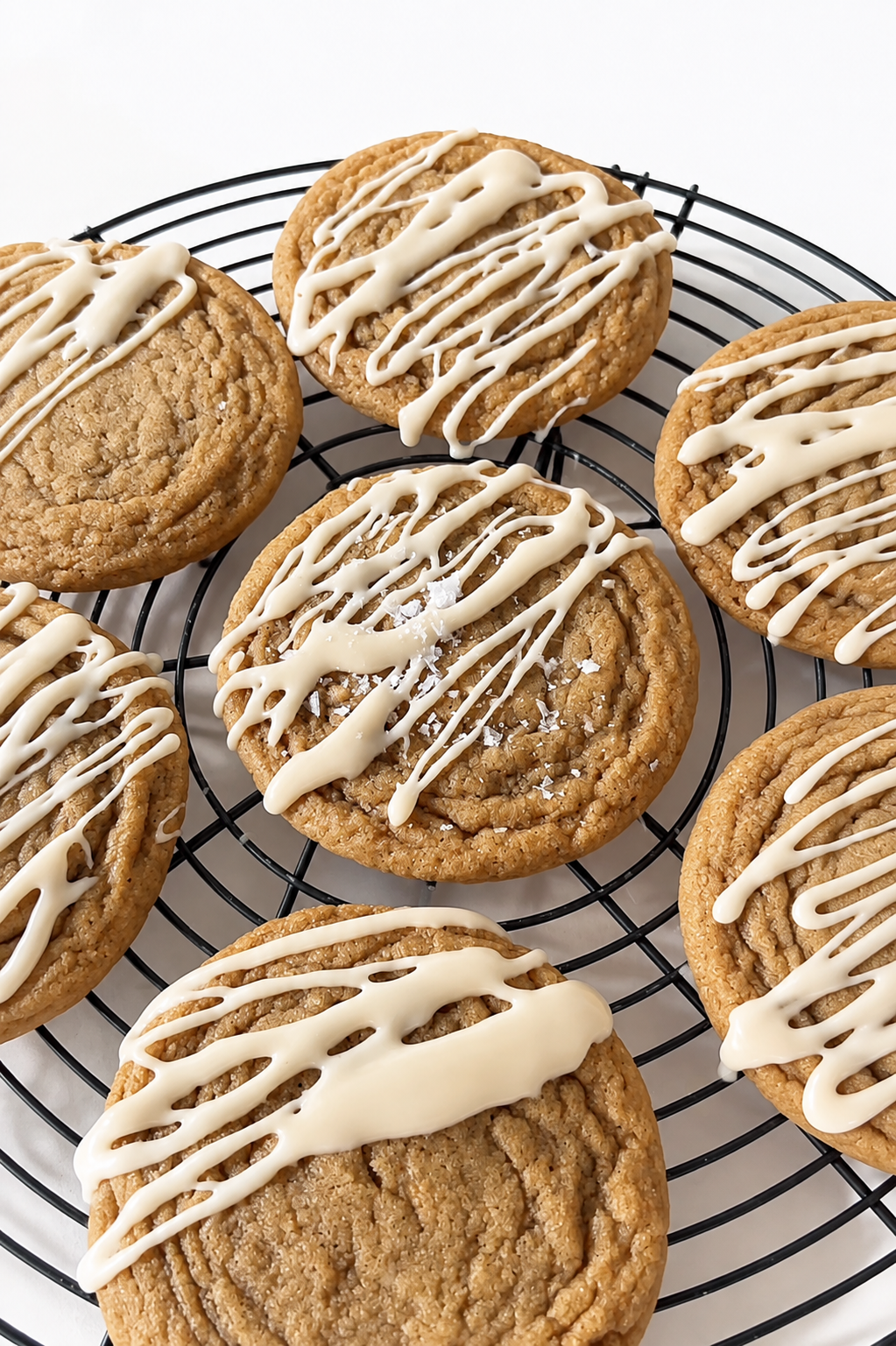Brown butter cookies with white chocolate drizzle and sea salt on a cooling rack